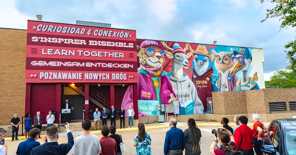 crowd of people viewing the unveiling of the Sister Cities mural on the side of Mounce Public Library 