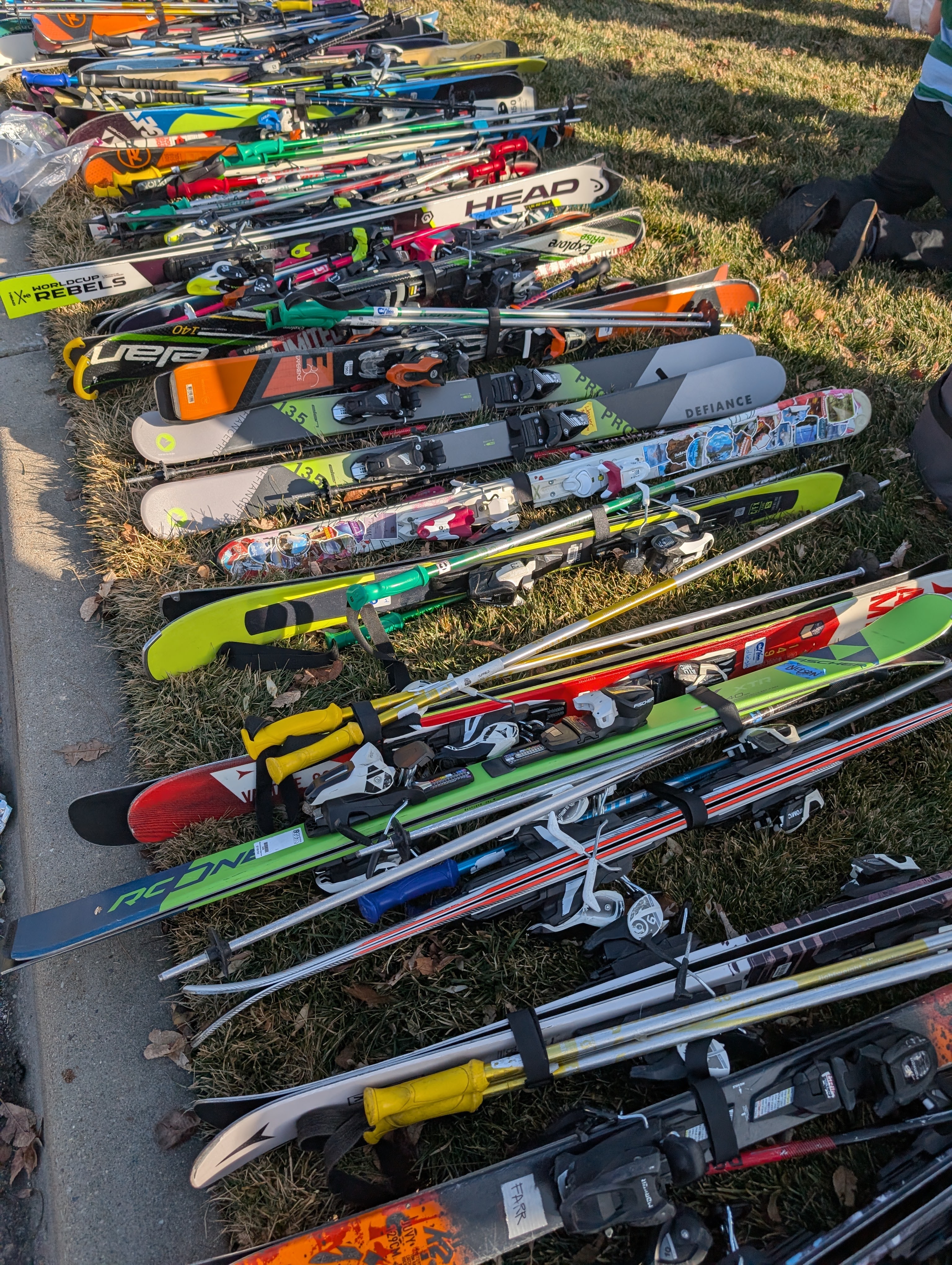 Bunch of skis bundled with pole lined up on the grass waiting to be loaded into ski bus