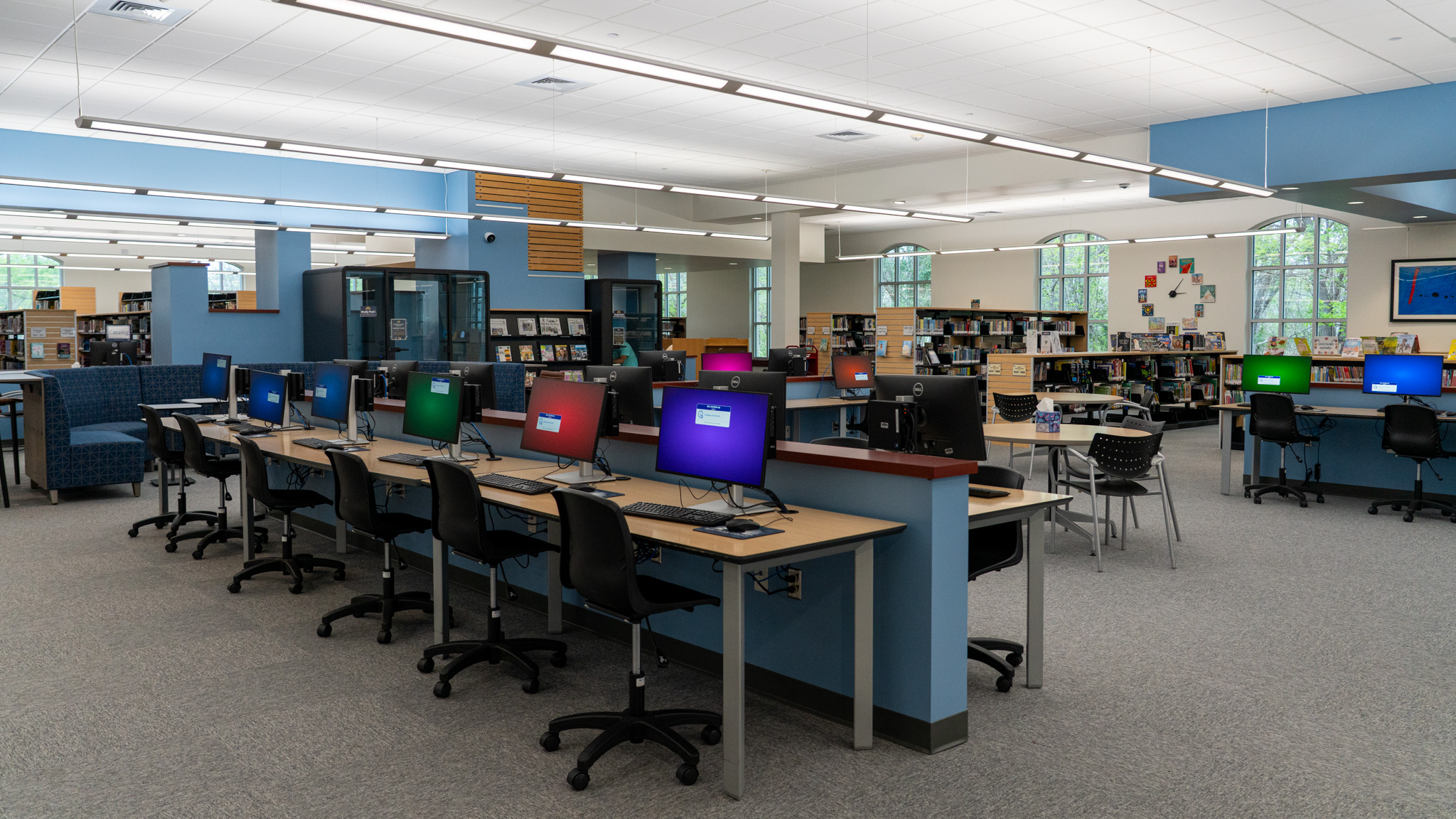 rows of computer monitors on a table in the middle of the library