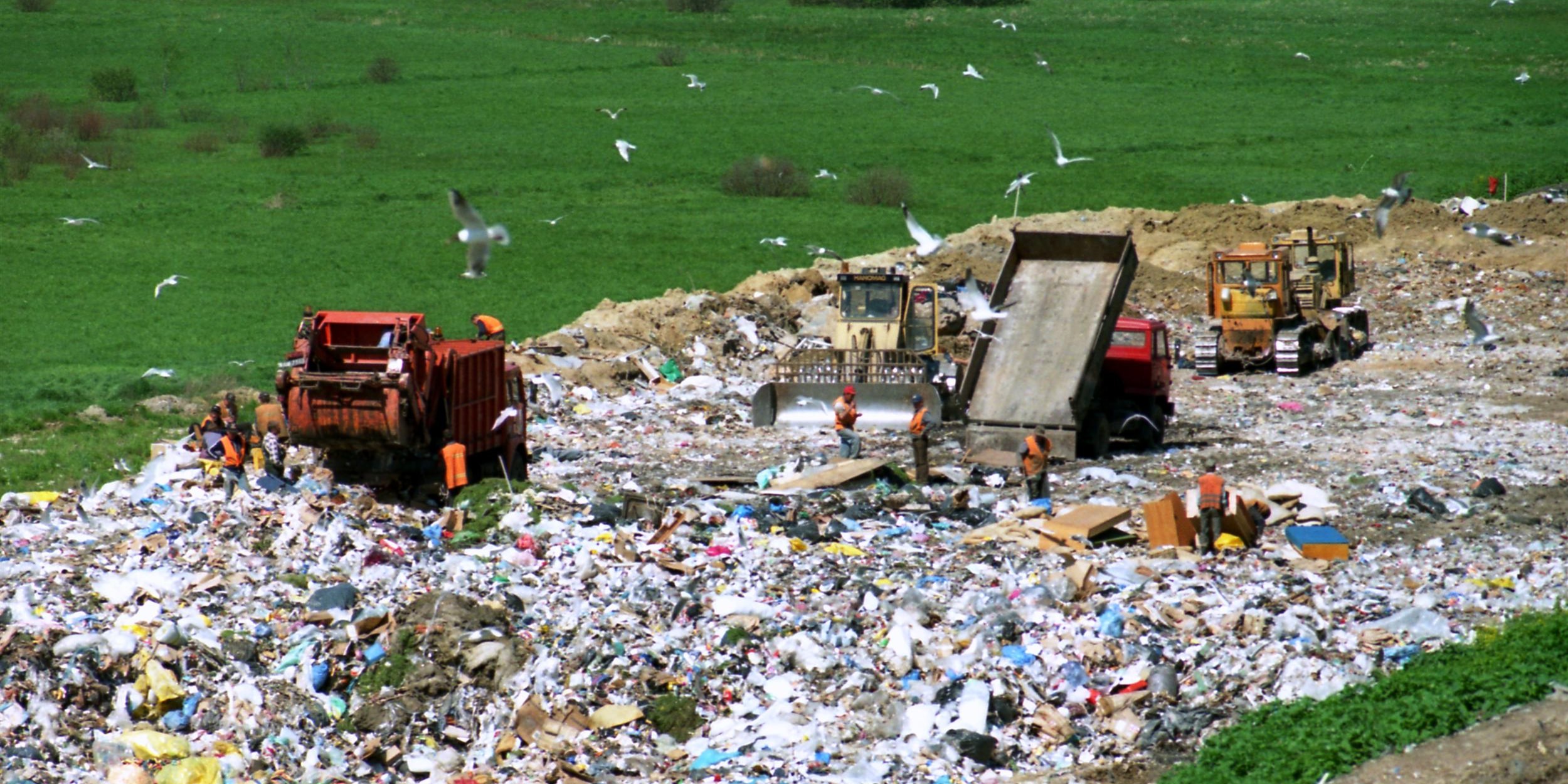 Bulldozers, dump trucks, and compactors are working on an active landfill.