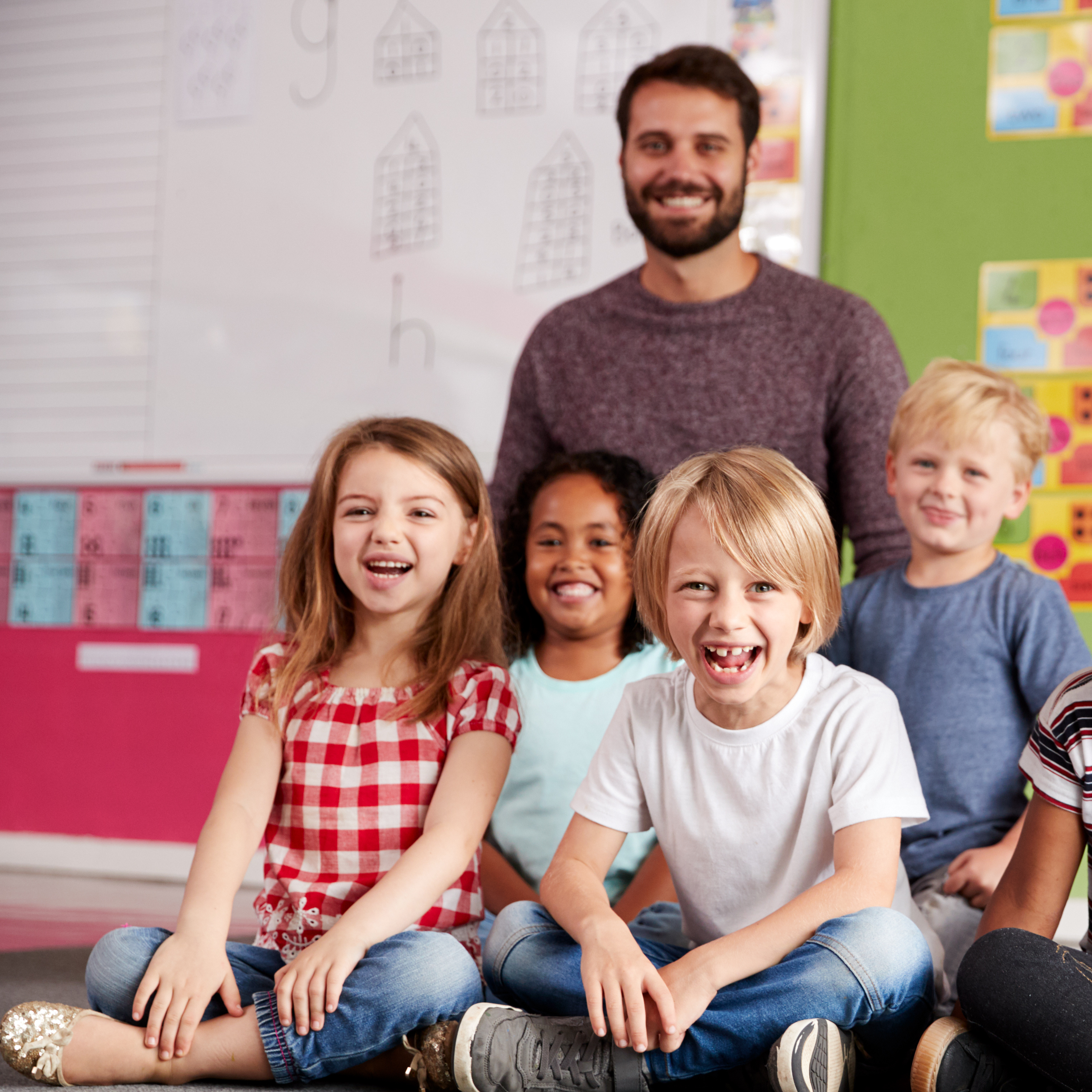 Teacher standing behind smiling young students seated on the floor