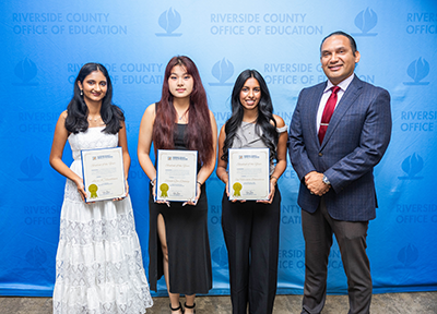 Three young women holding honors standing with superintendent