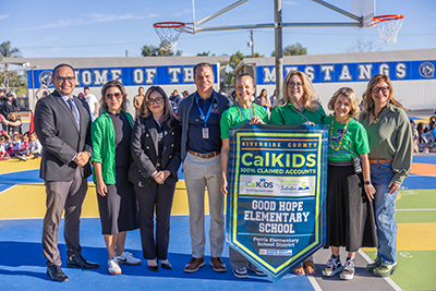 Educators standing on basketball court at home of the mustangs holding a CalKIDS banner for Good Hope Elementary School