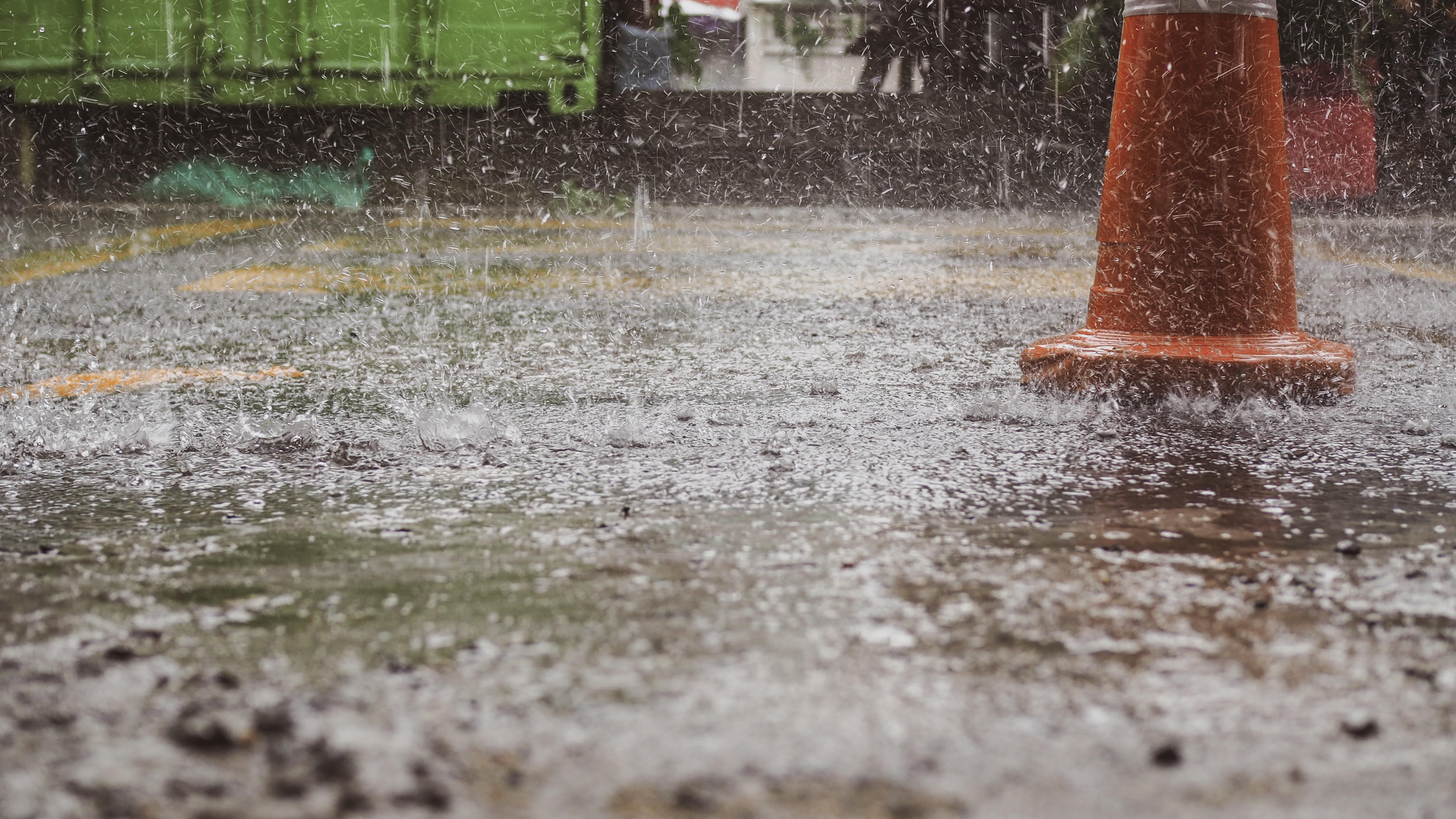 An orange traffic cone on an asphalt road with rain coming down.