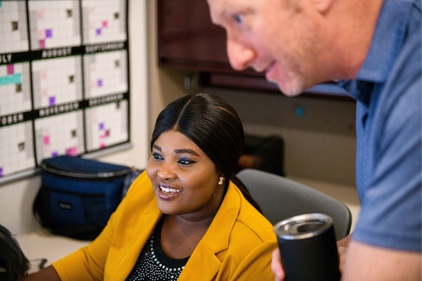 a woman smiling at a computer off screen with a man leaning over out of focuse