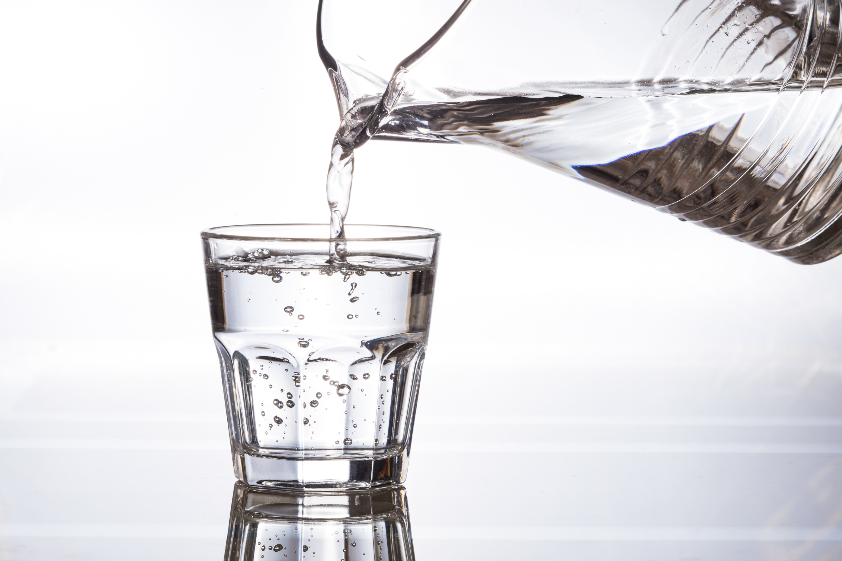 a clear glass being filled with water from a pitcher