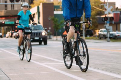 Two cyclists riding in bike lanes next to vehicles in the drive lanes.