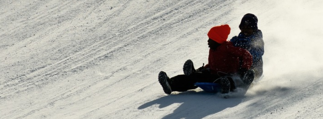 Two people sled down a snowy hill together.