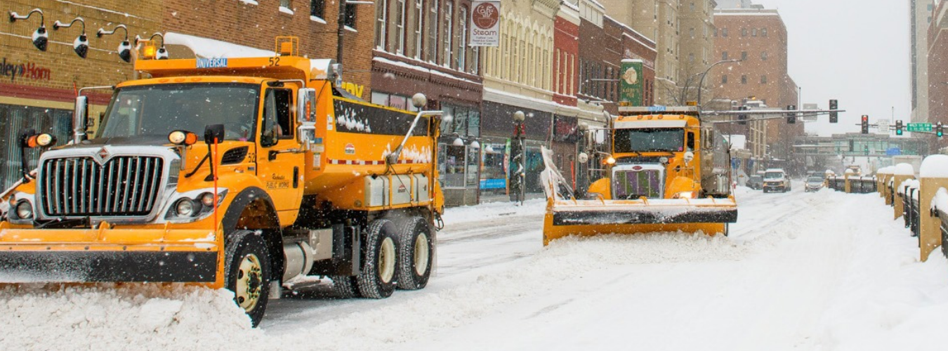 City snowplows clear snow from a downtown street during a winter storm.