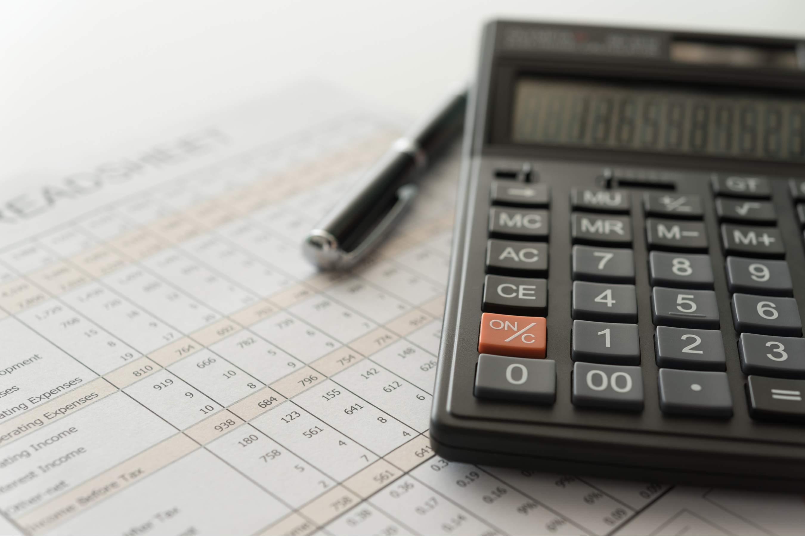 a calculator and pen resting on an unidentifiable data sheet